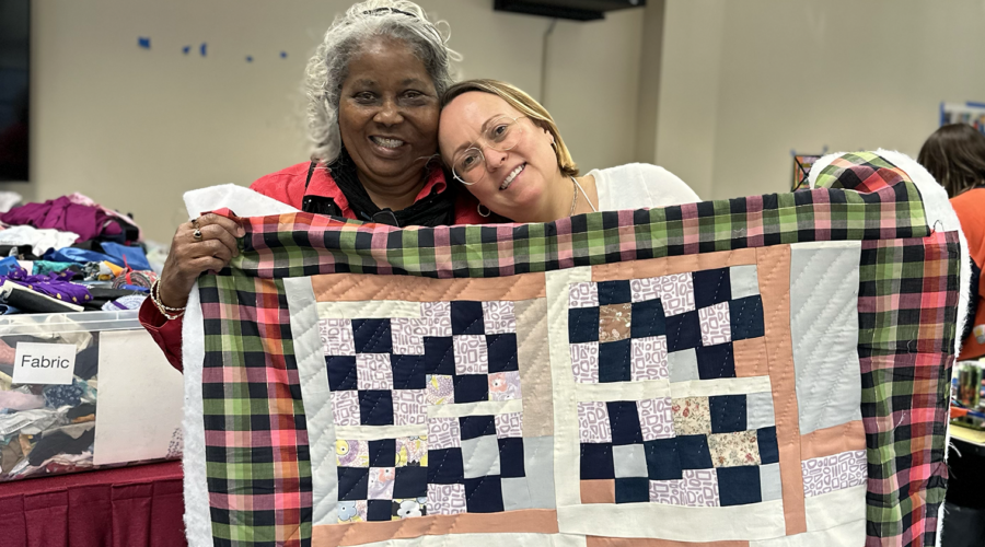 image of two women smiling and holding up a colorful patchwork quilt at Gee's Bend